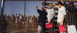 Grupo de deportados aguarda junto a cerca que separa San Diego, nos EUA, e Tijuana, no México.